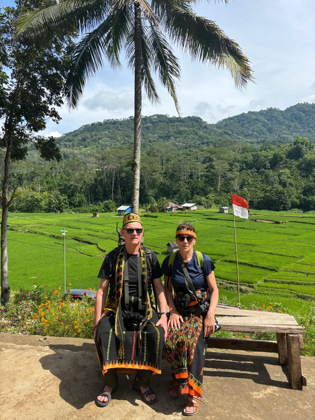 Guests in traditional Manggarai dress at a village welcome, rice fields behind
