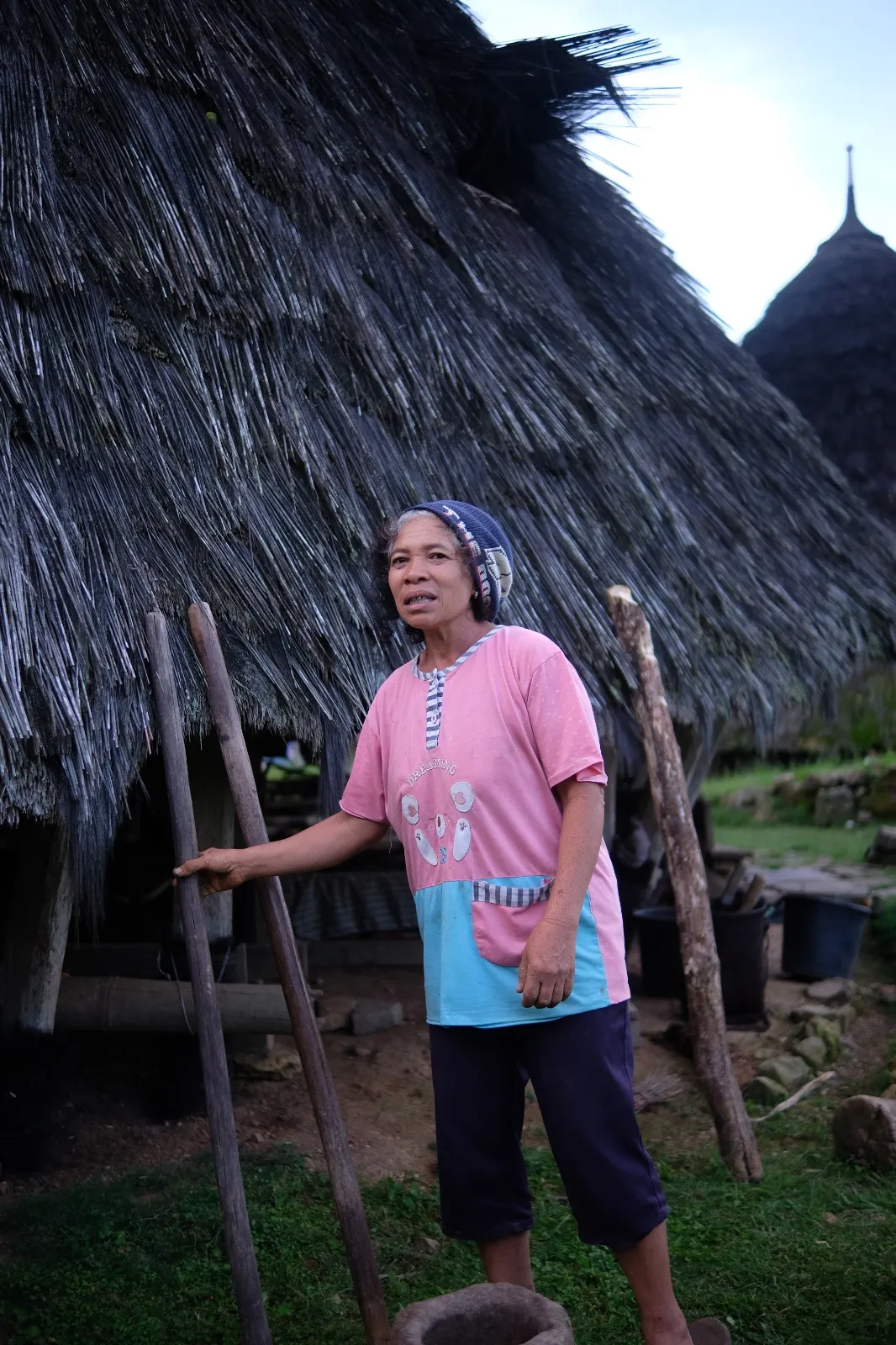 A Wae Rebo villager in traditional dress beside a thatched house
